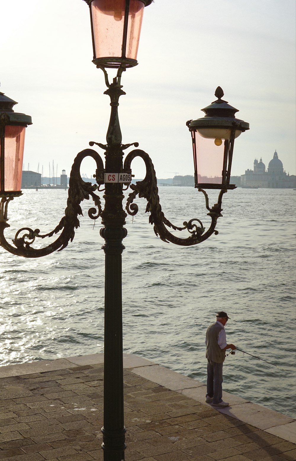 a man standing next to a lamp post by the water