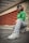 A person is crouching on an urban street, dressed in a vibrant green shirt, zebra-striped pants, and white sneakers. They wear stylish white sunglasses and have their hair styled in cornrows and loose bangs. The background features red industrial vents and a concrete building, with green graffiti visible on the wall.