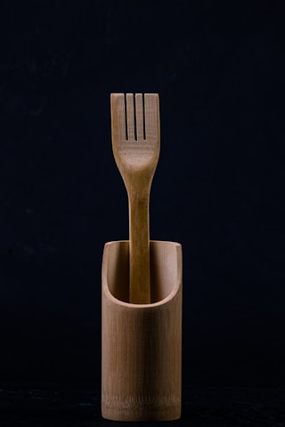 A wooden fork is elegantly placed inside a matching wooden container. The background is dark, emphasizing the natural texture and simplicity of the design.