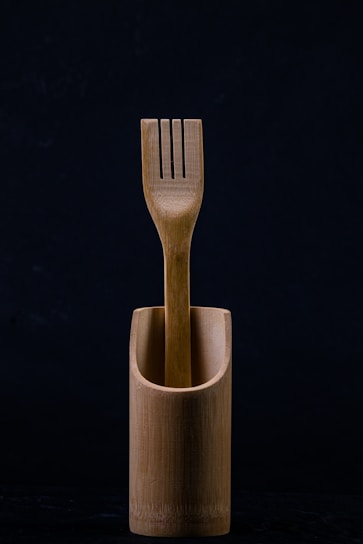 A wooden fork is elegantly placed inside a matching wooden container. The background is dark, emphasizing the natural texture and simplicity of the design.