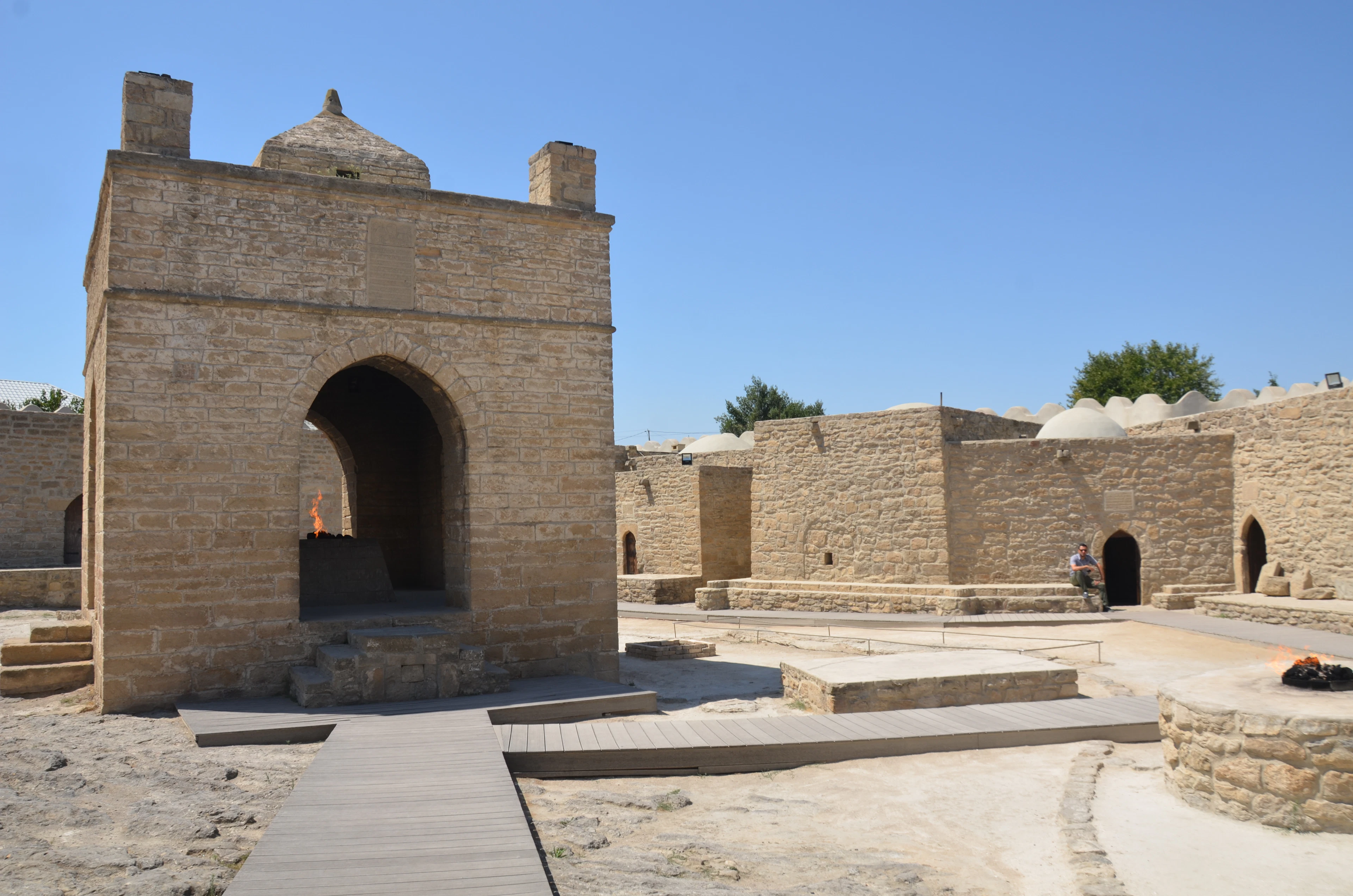 The Ateshgah fire temple outside Baku, its square stone altar pavilion burning a natural gas flame under the central arch, ringed by the low domed cells of the pentagonal caravanserai under a hard blue sky