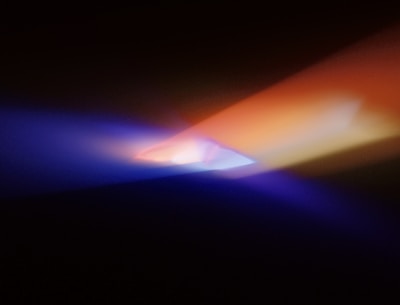 Beams of light in shades of blue, orange, and purple converge in a darkened space, creating an abstract, mystical effect.