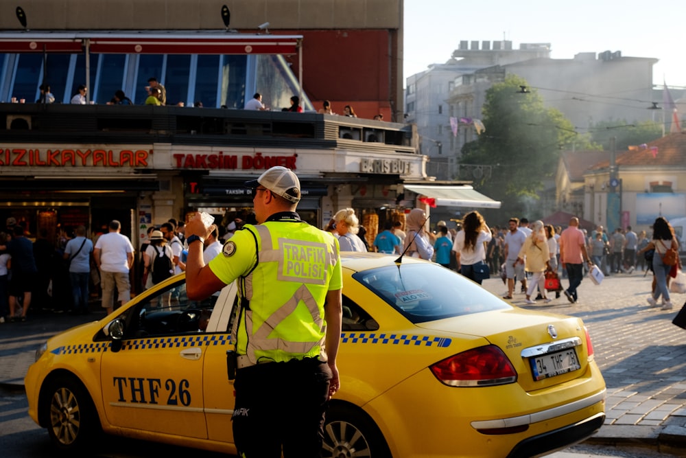 Una persona parada junto a un coche amarillo con una multitud de personas