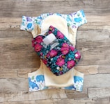 A reusable cloth diaper with a vibrant floral pattern on an outer layer is laid out. Beneath it is another diaper with a design featuring various colorful animal illustrations such as elephants and dinosaurs. These are set against a rustic wooden background.