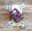 A reusable cloth diaper with a vibrant floral pattern on an outer layer is laid out. Beneath it is another diaper with a design featuring various colorful animal illustrations such as elephants and dinosaurs. These are set against a rustic wooden background.