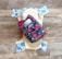 A reusable cloth diaper with a vibrant floral pattern on an outer layer is laid out. Beneath it is another diaper with a design featuring various colorful animal illustrations such as elephants and dinosaurs. These are set against a rustic wooden background.