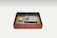 An ornately decorated box with an intricate red design holds a rectangular stone ink slab and a small, round lid with gold accents. The items are neatly placed inside the box, which features a black interior.