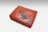 An intricately designed rectangular box with carvings on the top surface, featuring various figures and decorative patterns. The box has a predominantly red hue with some darker accents in the carvings.