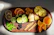 A rustic wooden tray displaying an assortment of colorful dry fruits and seeds.