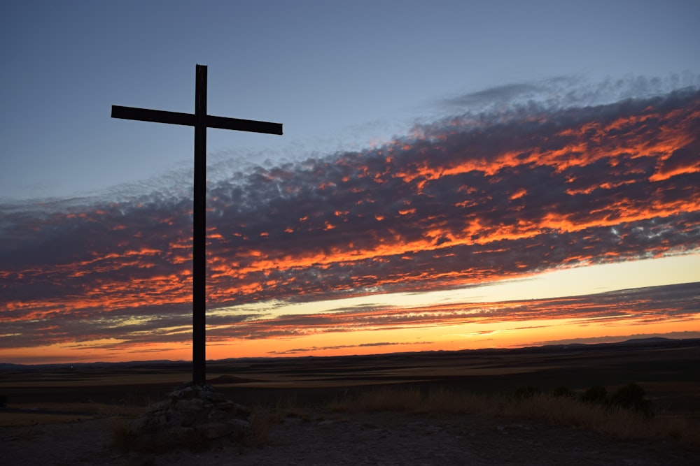 une croix sur une colline avec un coucher de soleil en arrière-plan