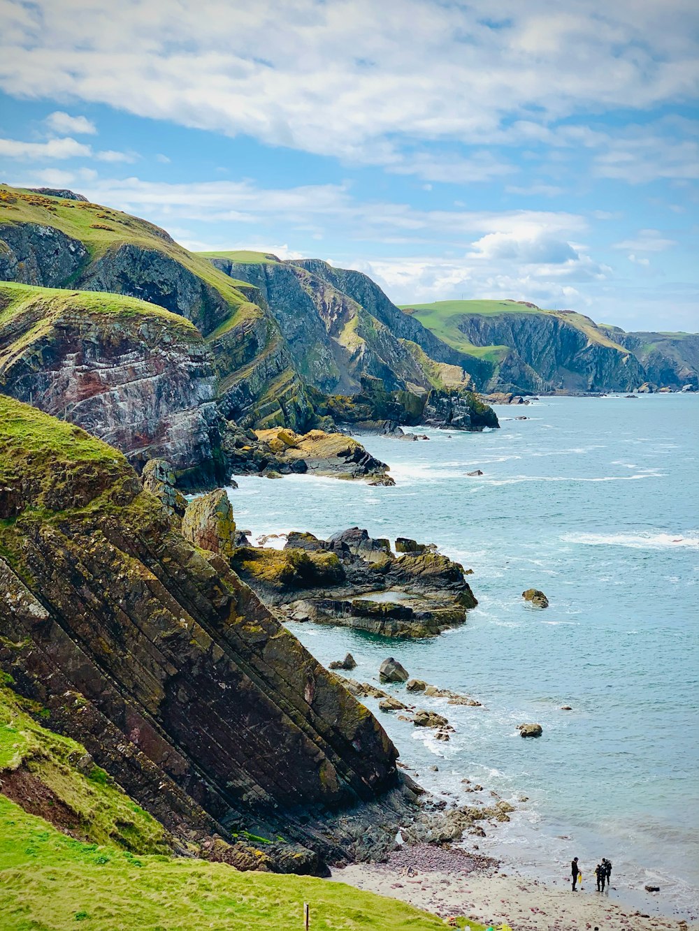 a rocky beach with a body of water and mountains in the background