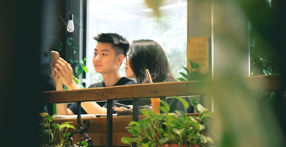 a man and woman sitting at a table with plants and a window