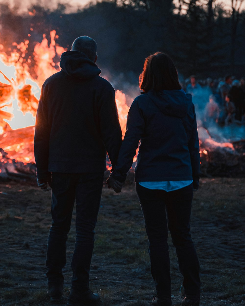 a man and woman standing in front of a large fire