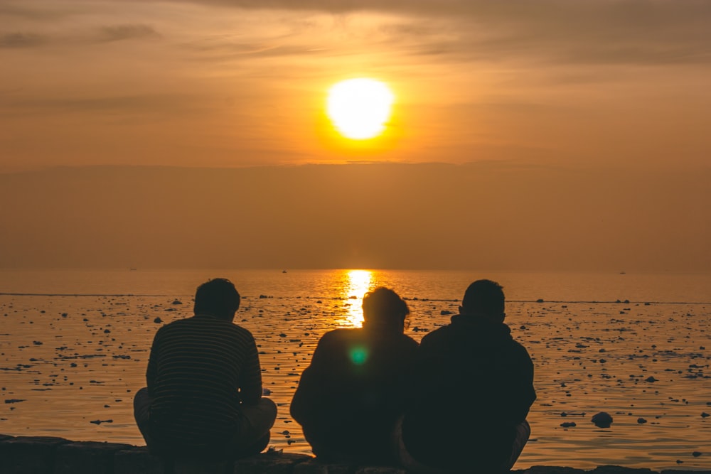 a group of people sitting on a beach looking at the sunset