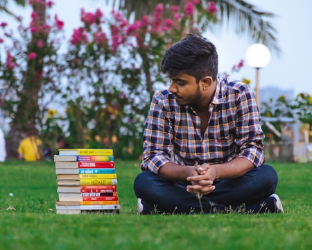 a person sitting on grass with stacks of books