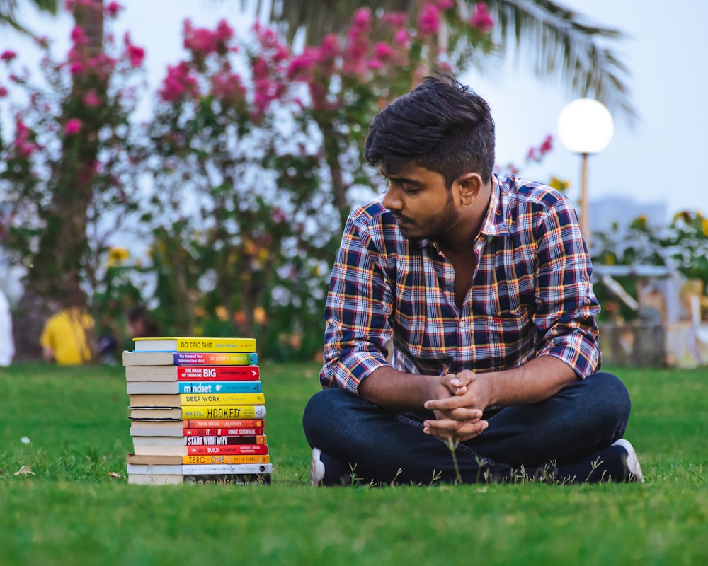 a person sitting on grass with stacks of books