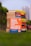 A stack of self-help books arranged outdoors, with vibrant covers. The central focus is on 'How to Win Friends and Influence People' prominently displayed in the foreground. The books are placed on lush green grass, with blurred city buildings in the background.