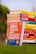 A stack of colorful self-help and motivational books is placed on grass, with titles clearly visible. The books are arranged with one book prominently displayed in the foreground, titled 'How to Win Friends and Influence People'. The setting appears to be outdoors with a blurred backdrop of greenery and a clear sky.