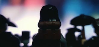 Silhouettes of LEGO figures in focus against a blurred multicolored background. The lighting creates a mysterious and dramatic atmosphere by casting shadows and highlighting the contours.
