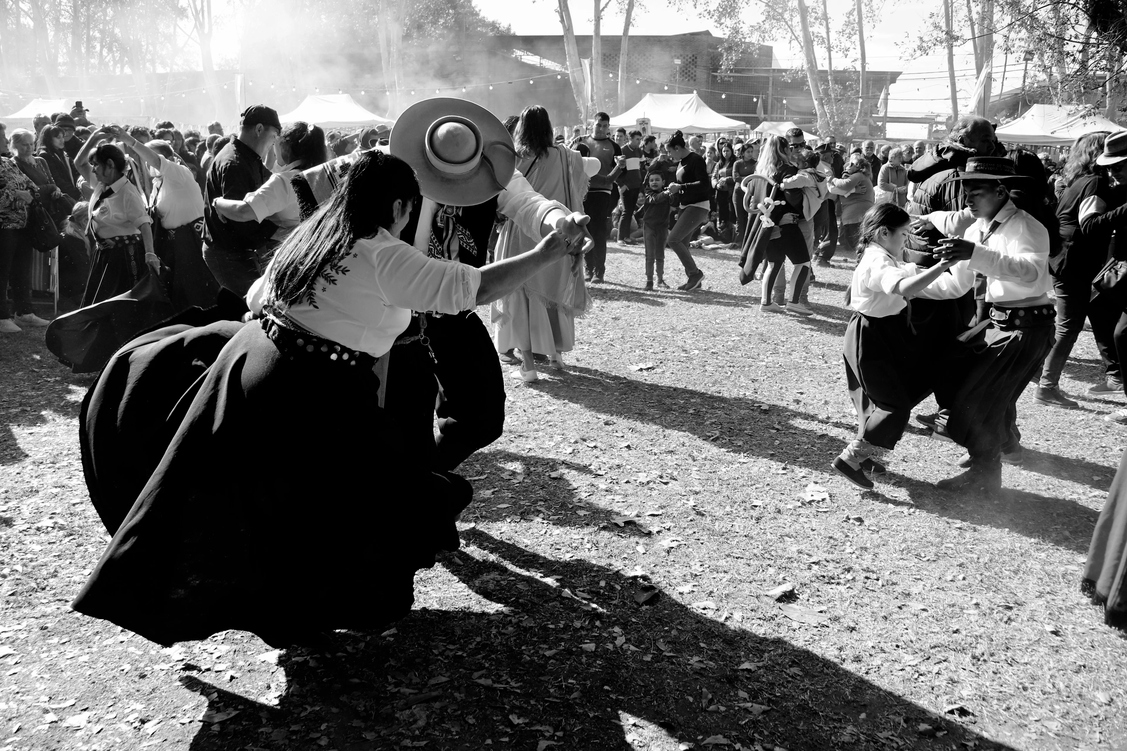 Parejas vestidas de paisanos bailando en una fiesta criolla, entre el polvo y el público