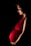 A pregnant woman stands gracefully, illuminated by soft lighting against a dark background. She wears a vibrant red dress that accentuates her belly, and a floral headpiece rests on her head. Her gaze is gentle and focused downward.