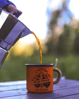 Freshly brewed coffee being poured into a ceramic cup, with the backdrop of Hunza mountains visible through the café window.