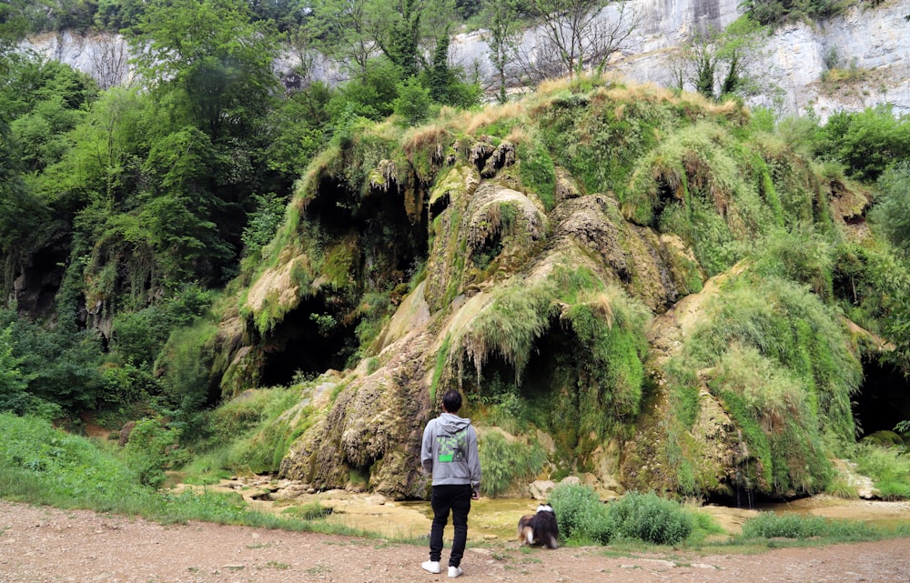 a person and a dog walking on a dirt path in front of a large rock formation