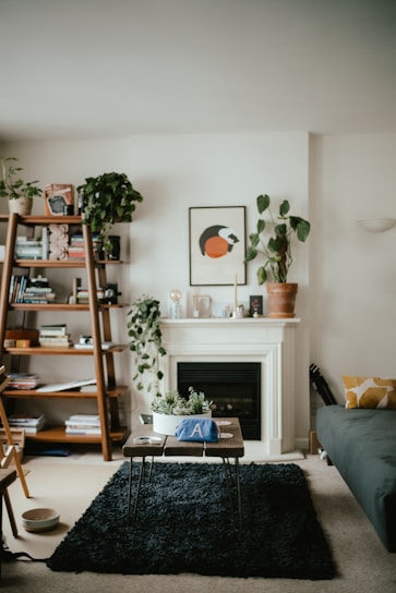 A cozy living room featuring a minimalist solid wood bookshelf filled with colorful books and decorative plants.
