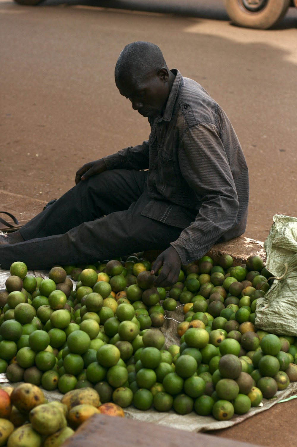 a man squatting down next to a pile of green fruit