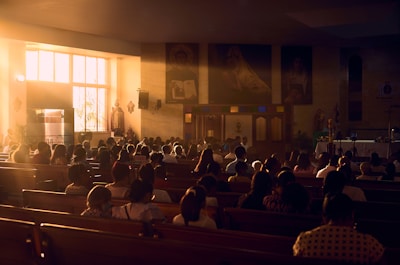 a group of people sitting in a room with a stage and a large screen