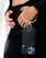 A person is holding a sleek black phone case with a gold metallic wristlet attached. The focus is on the elegant accessory, which contrasts against a black outfit. The person's hands are gently positioned near the waist, adding to the sophisticated appearance.