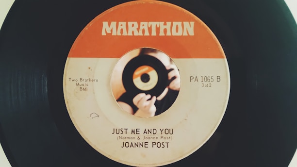 A vintage vinyl record with a label design featuring an orange and white color scheme. The label shows the song title 'Just Me and You' by Joanne Post and includes details like 'Two Brothers Music BMI' and 'PA 1065 B.' There is a central image of hands holding a small record.