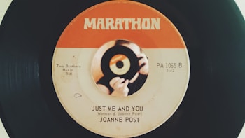 A vintage vinyl record with a label design featuring an orange and white color scheme. The label shows the song title 'Just Me and You' by Joanne Post and includes details like 'Two Brothers Music BMI' and 'PA 1065 B.' There is a central image of hands holding a small record.