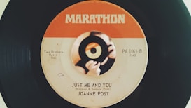 A vintage vinyl record with a label design featuring an orange and white color scheme. The label shows the song title 'Just Me and You' by Joanne Post and includes details like 'Two Brothers Music BMI' and 'PA 1065 B.' There is a central image of hands holding a small record.