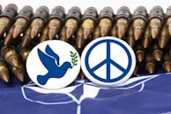 Two buttons are placed in front of a row of bullets. One button features a blue dove holding a green olive branch, while the other displays a blue peace symbol. The background includes a fragment of a flag.