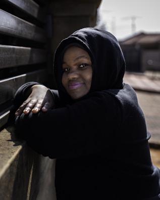A relaxed model lounging in a soft Lazy Legend Club hoodie against a sunlit urban backdrop.