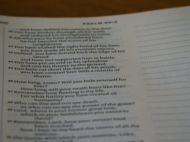 A close-up of an open book displaying a passage from the Bible. The text is printed in black ink on white paper, with some lines highlighted in bold. A dotted line is visible on the right side of the page.