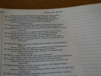 A close-up of an open book displaying a passage from the Bible. The text is printed in black ink on white paper, with some lines highlighted in bold. A dotted line is visible on the right side of the page.