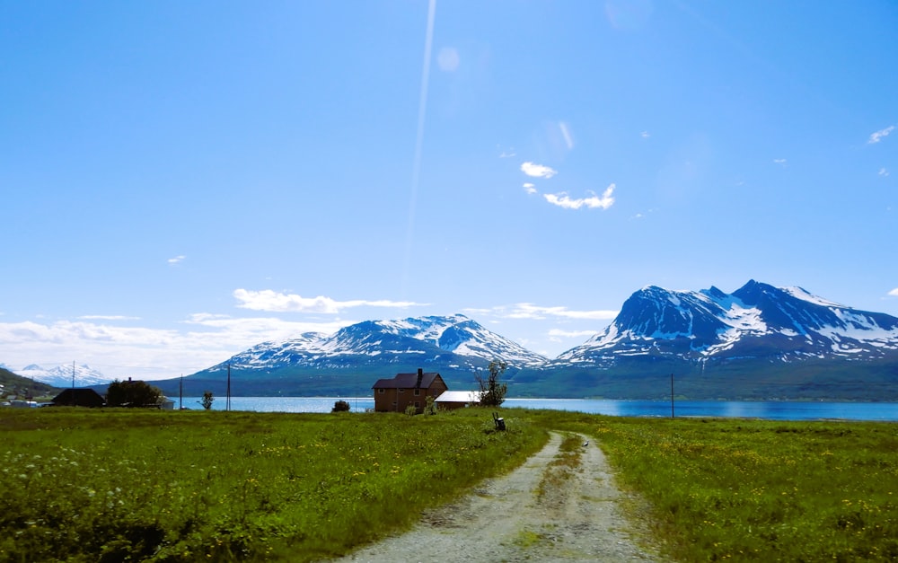 a dirt road leading to a house and snowy mountains