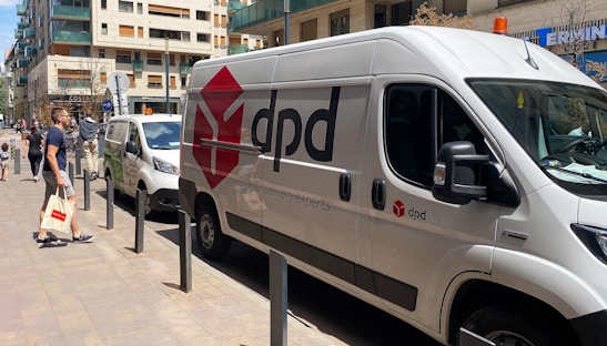 Delivery van parked outside a modern office building with a driver preparing parcels.