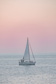 A serene sailboat gliding over calm turquoise waters at sunset.