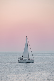 A serene sailboat gliding on calm blue waters at sunset.