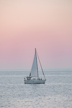 A serene sailboat gliding over calm turquoise waters at sunset.