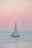A serene sailboat gliding through calm Venetian lagoon waters at sunset.