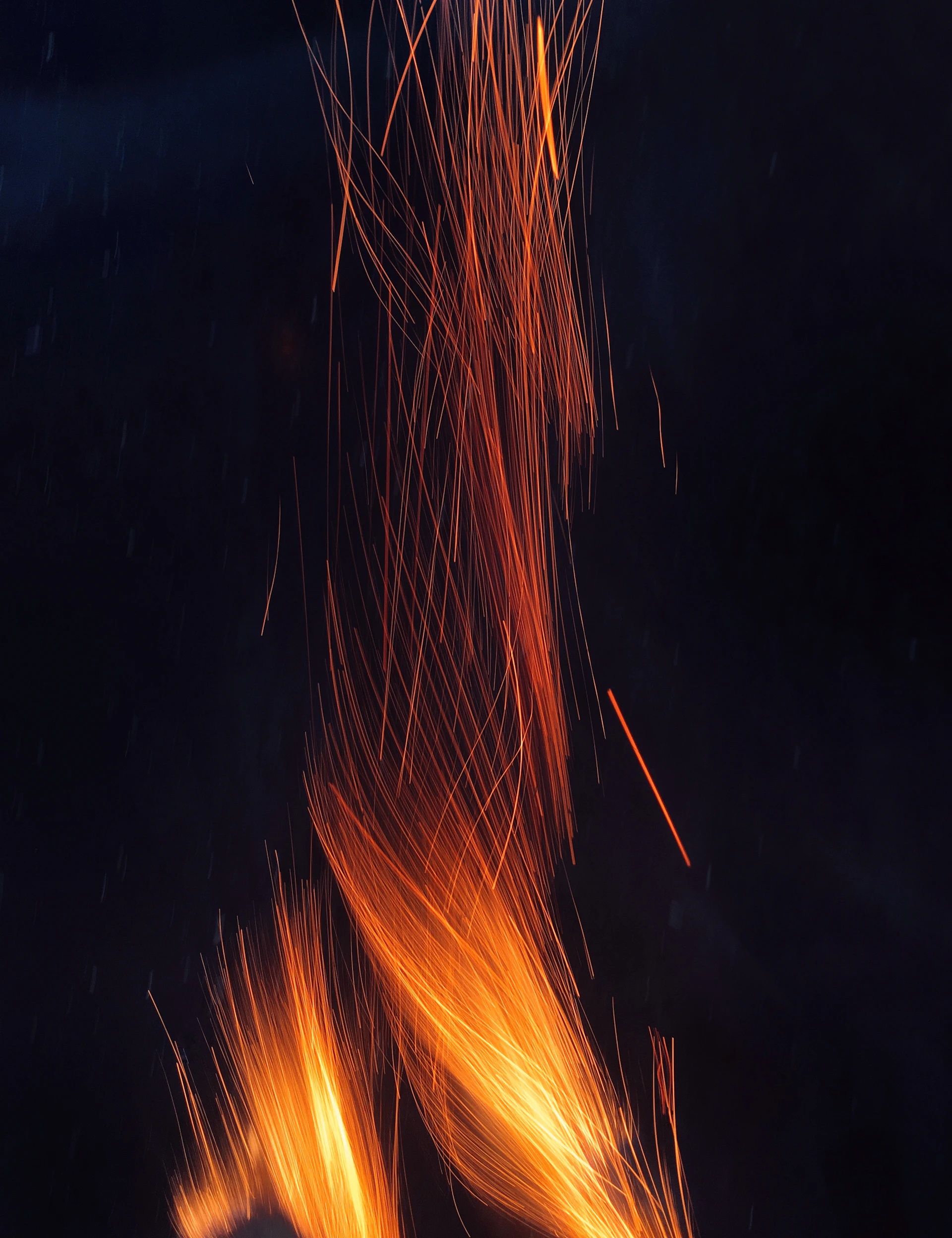 Bright orange sparks rising in long vertical streaks against a dark night sky