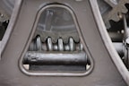 Close-up view of a mechanical gear system, featuring large metal components with visible gears and axles. The metal surfaces are painted in a matte gray color, with signs of wear and some accumulated grease at the joints.