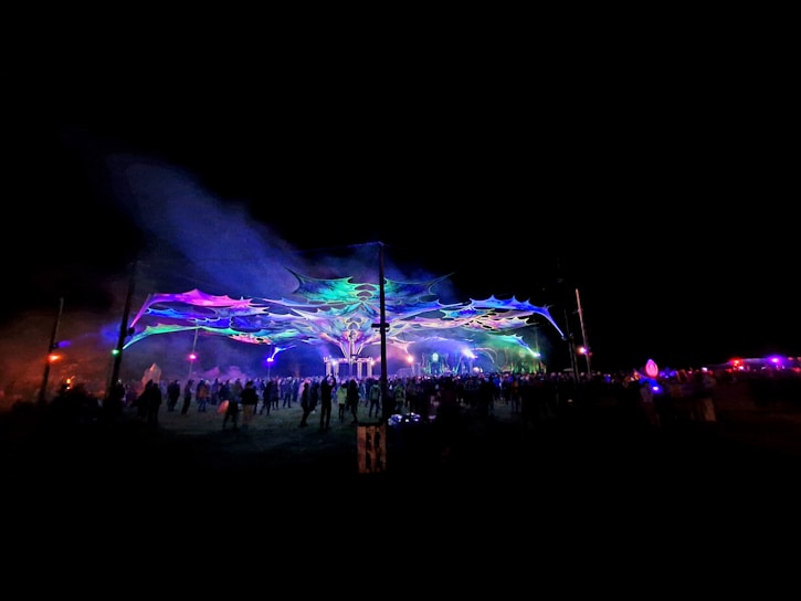 A vibrant crowd dancing under colorful festival lights at night.