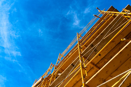 Close-up of sturdy yellow scaffolding set against a clear blue sky at a busy construction site.