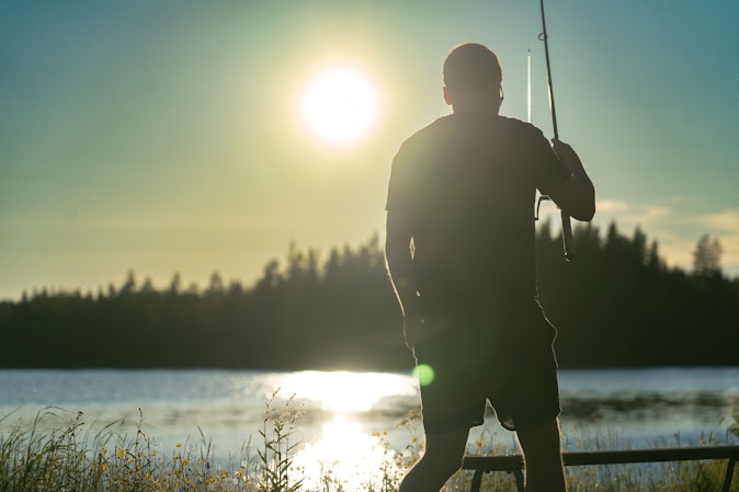 a person fishing on a lake in the summer sun