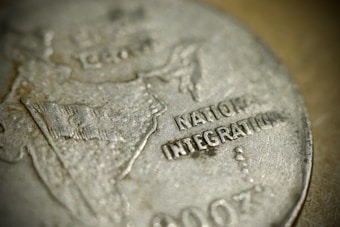 A close-up view of a coin displaying the map of India and the text 'NATIONAL INTEGRATION.' The coin's surface is metallic with embossed text and symbols.